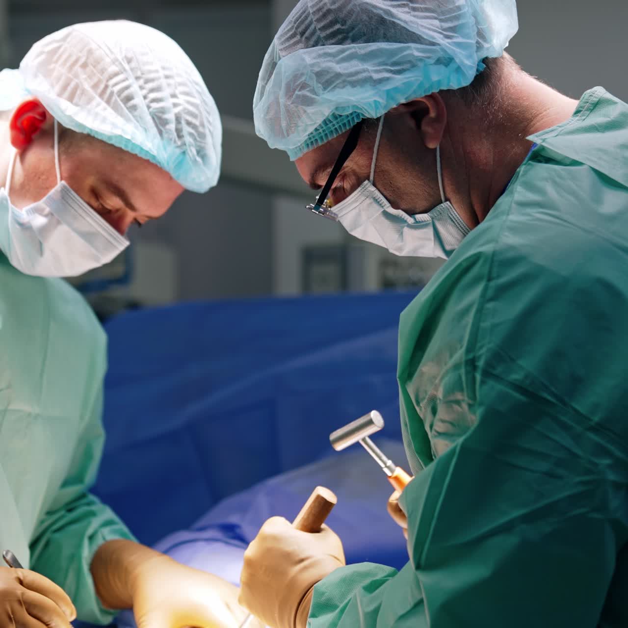 Chirurgo maschio indaffarato chinato sul paziente sul tavolo operatorio. Il medico principale applica martello e scalpello.