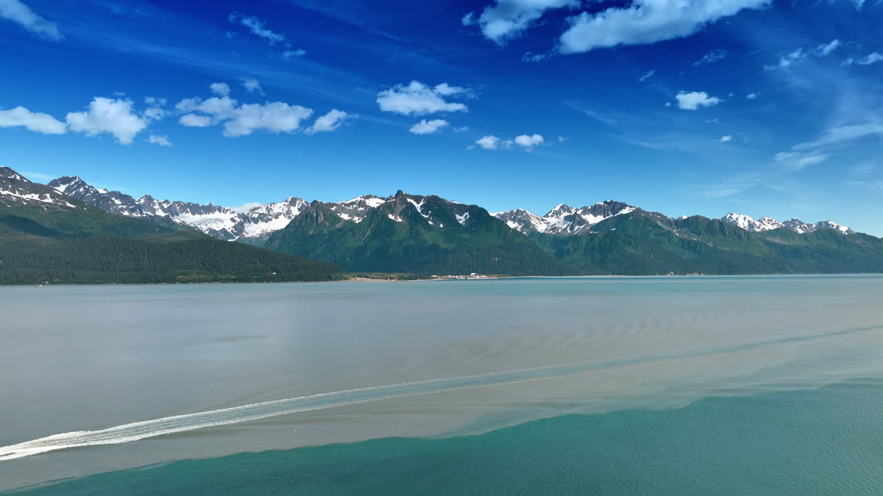 Peaceful vast waterscape at the foot of the mountain range. Small fluffy clouds are in the blue sky. Alaska, USA