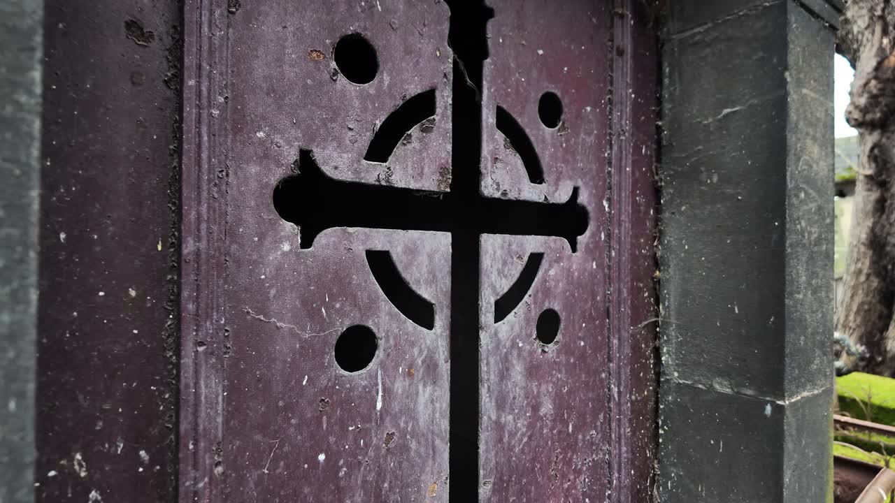 パリの墓地にある、十字架のシンボルが施された装飾的な霊廟の地下室の扉。風化した金属と石の建築様式が特徴で、歴史的または宗教的なテーマに最適。