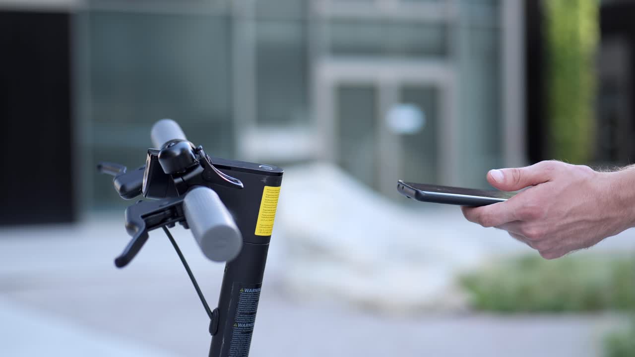 Hand holding a smartphone next to an e scooter to activate it close up