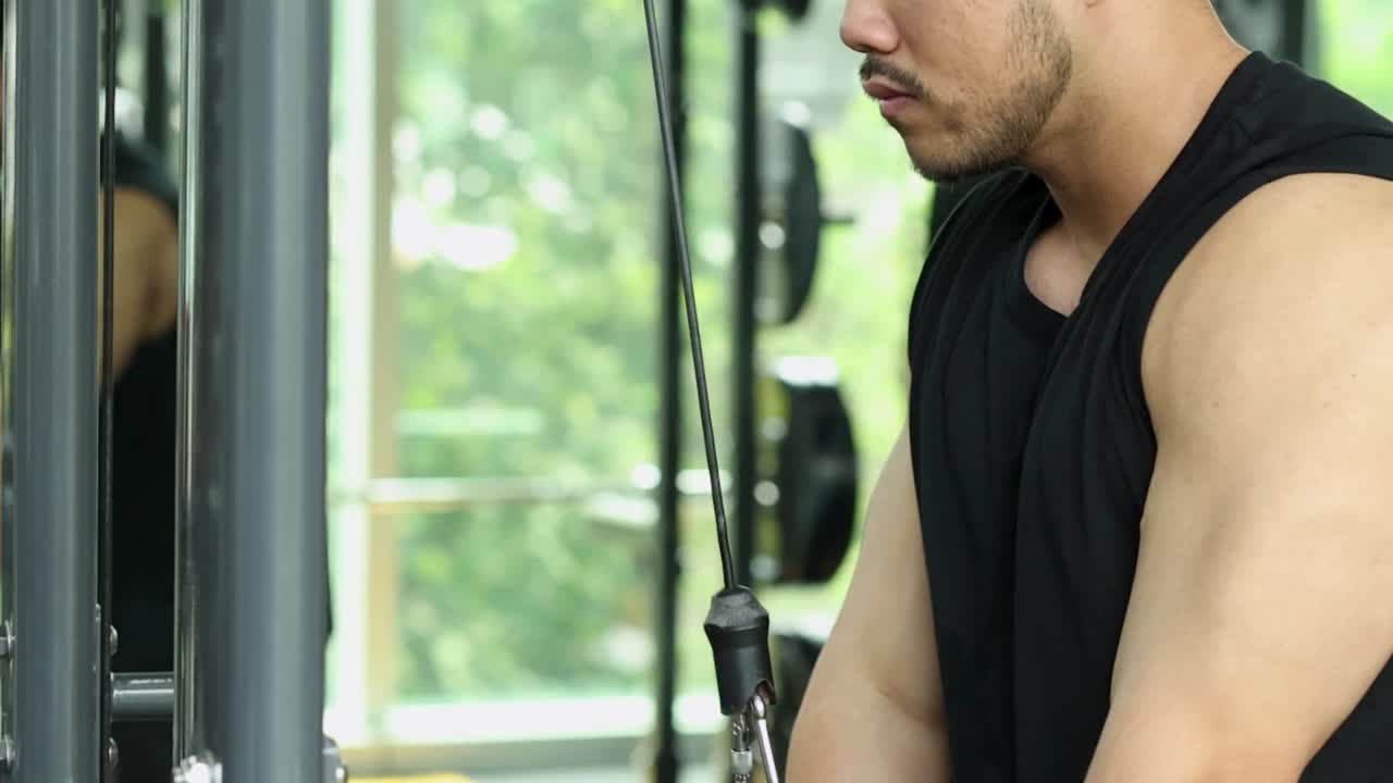En fokusert mann i en svart tanktopp utfører triceps pushdowns ved hjelp av en kabelmaskin