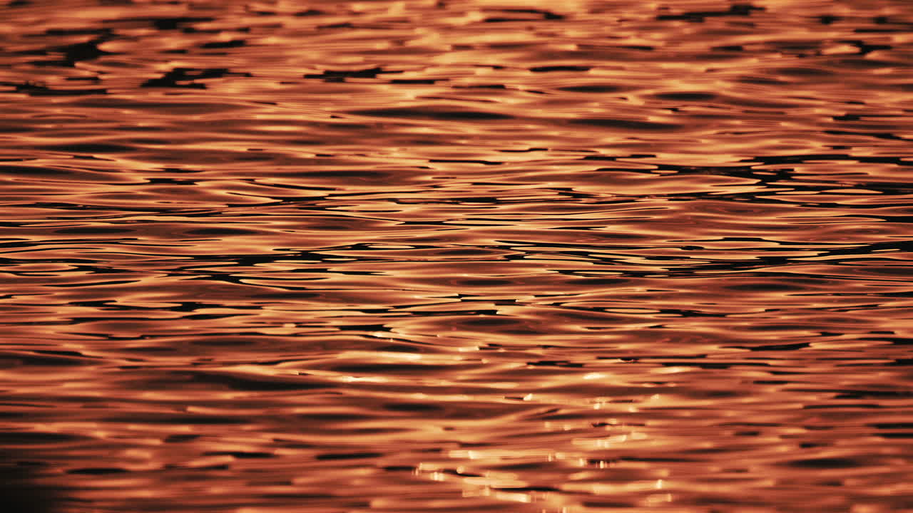Primo piano di riflessi arancioni e dorati del tramonto che si muovono su dolci increspature dell'acqua