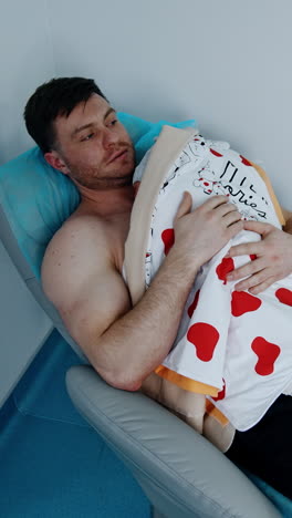happy caucasian male lies on the armchair holding his newborn child on the chest. skin-to-skin practice for a baby after c-section operation. vertical video