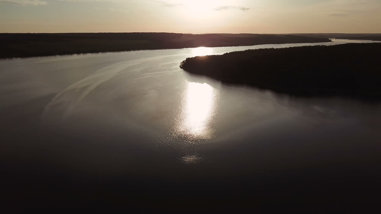 wide river is flowing at sunset in the summer. Sun's rays are reflecting in the water of the lake. Aerial view