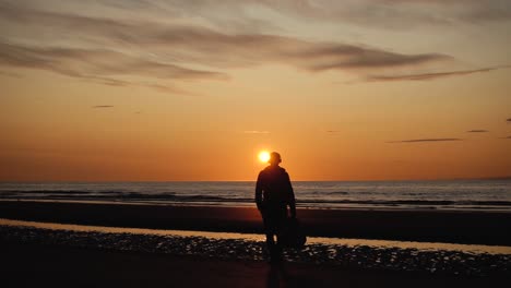 hombre corriendo con guitarra en la playa de arena trasera al atardecer