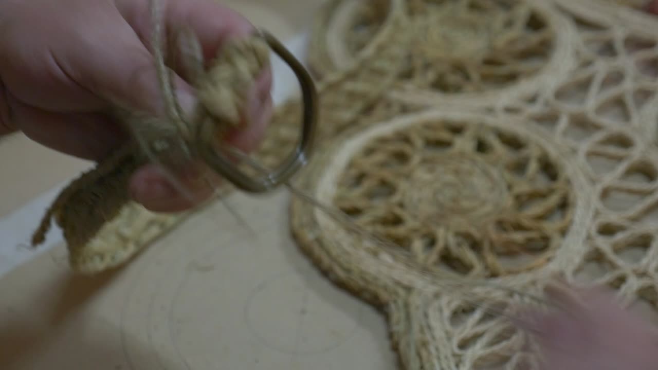 An artisan's hands weaving a strap with esparto rope. He uses a thick needle to pass the thread through the natural fiber