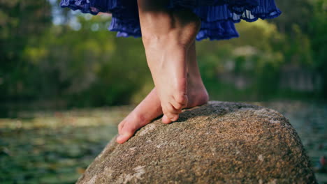 Woman bare legs standing big stone in front pond covered water lilies close up.