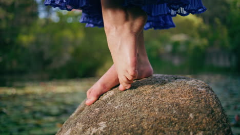 woman bare legs standing big stone in front pond covered water lilies close up.