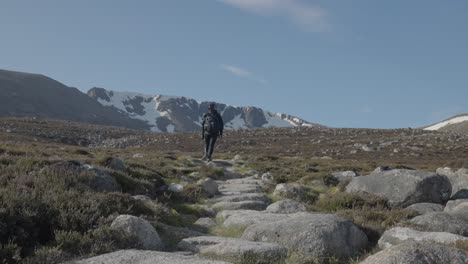 wide shot of woman walking toward snow capped scotland mountain peak with rocky trail as leading lines