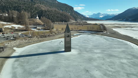 Drohnen-Dolley-Aufnahme-Zur-Versunkenen-Kirche-Von-Graun-Am-Reschensee-Mit-Alpen-Im-Hintergrund