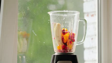 chunks of banana, mango and raspberries fall into blender for healthy smoothie