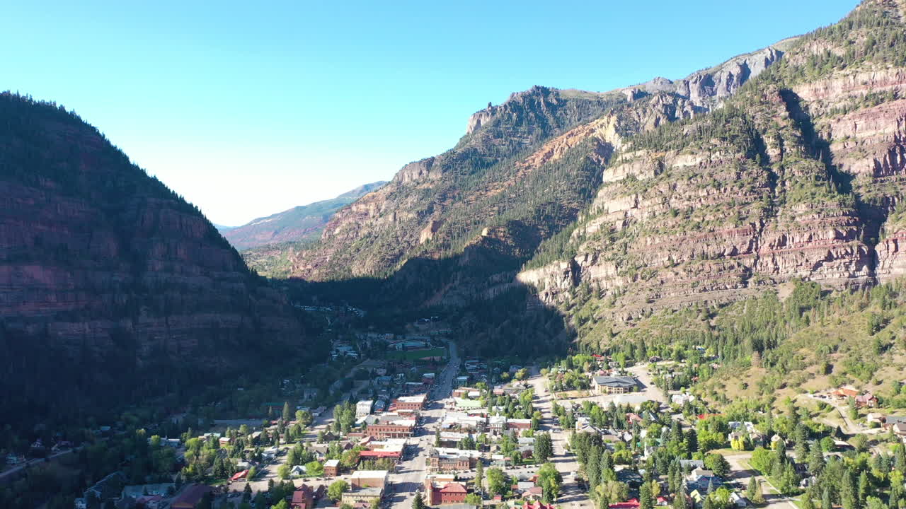 drones aéreos bajando el movimiento de la ciudad montañosa de ouray colorado, autos conduciendo por el centro y casas rodeadas de acantilados rocosos de montaña y sombra proyectada por la ciudad