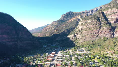 Drones-Aéreos-Bajando-El-Movimiento-De-La-Ciudad-Montañosa-De-Ouray-Colorado,-Autos-Conduciendo-Por-El-Centro-Y-Casas-Rodeadas-De-Acantilados-Rocosos-De-Montaña-Y-Sombra-Proyectada-Por-La-Ciudad