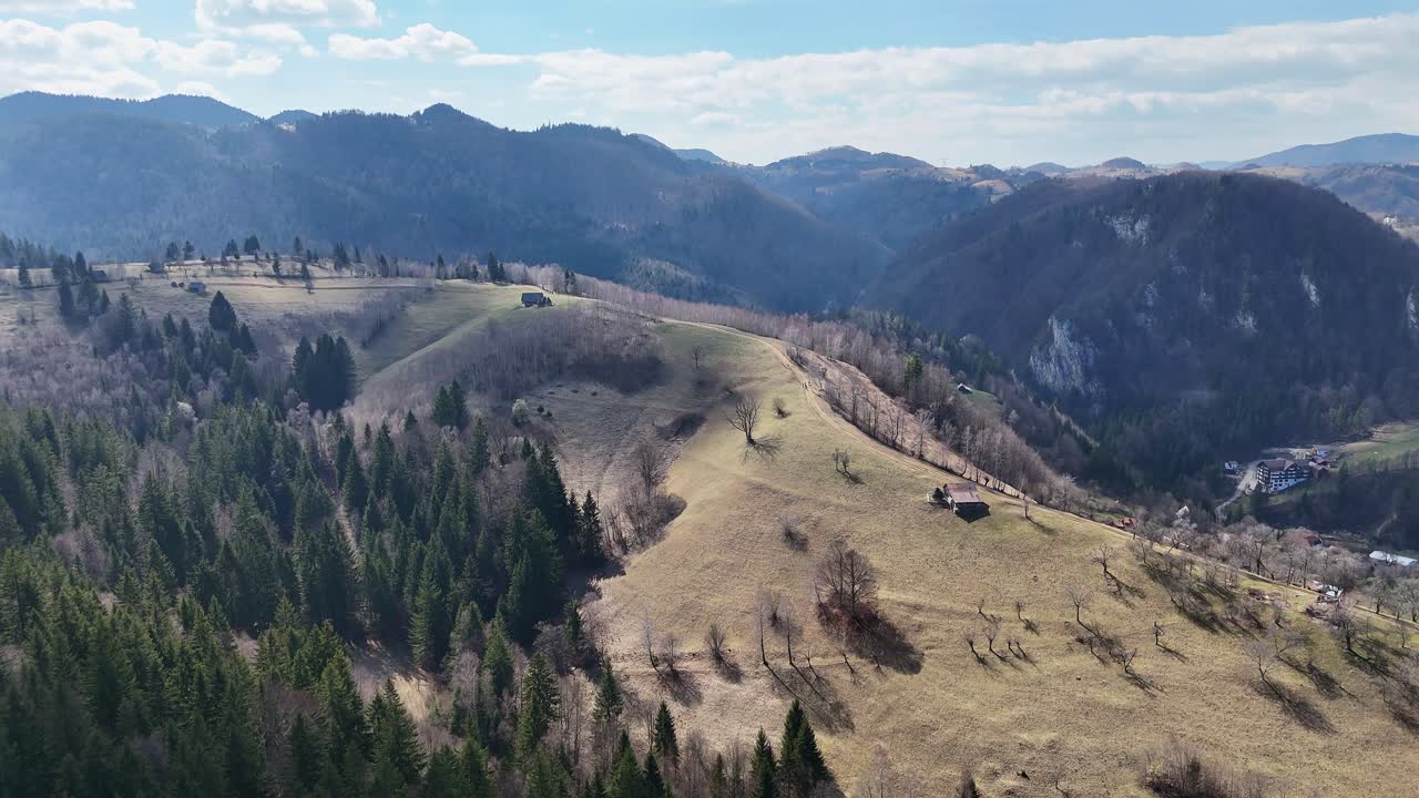 colinas onduladas y árboles esparcidos bajo un cielo despejado, con cadenas montañosas en el fondo