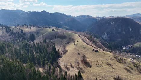 Rolling-hills-and-scattered-trees-under-a-clear-sky,-with-mountain-ranges-in-the-background