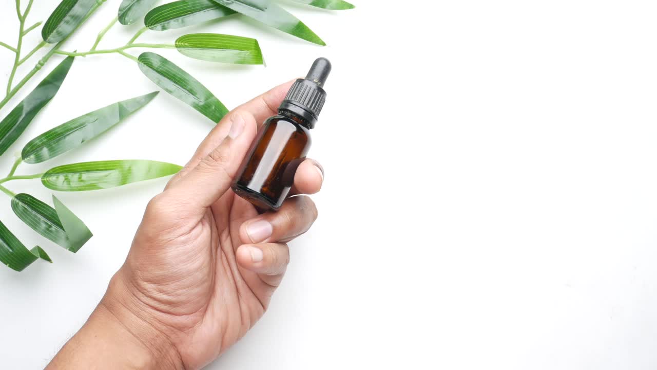 Hand Holding a Brown Glass Dropper Bottle with Green Leaves
