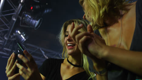 female friends reviewing pictures on mobile phone at a concert 4k