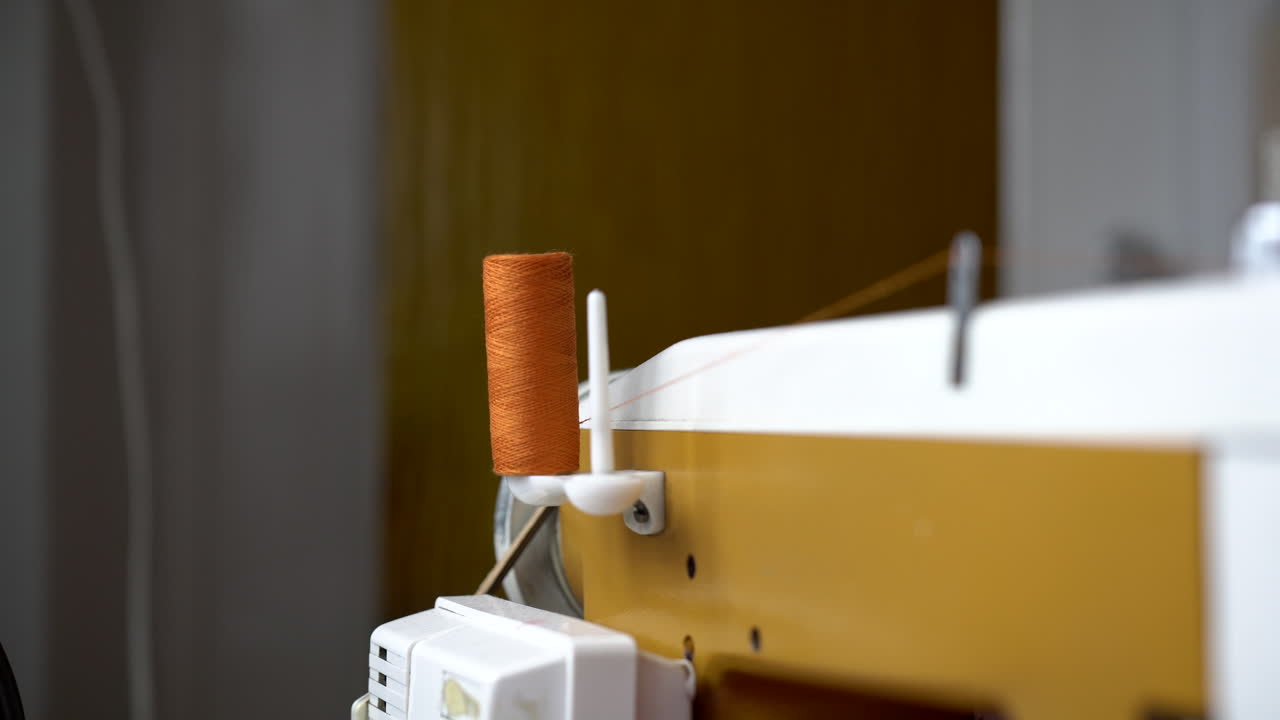 White sewing machine taking orange thread from the reel