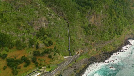 aerial top down shot of waterfall with driving car on coastal road on madeira island