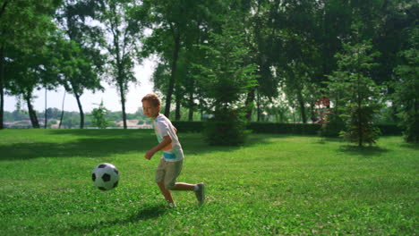 focused kid flicking up soccer ball. boy training on fresh air in summer park.