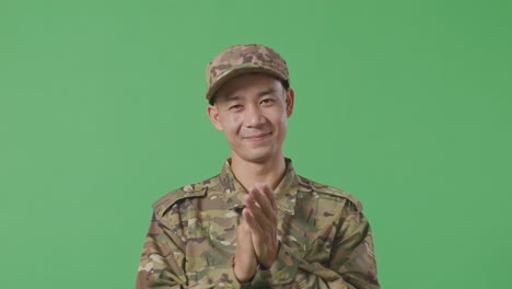 close up of asian man soldier smiling and clapping his hands while standing in the green screen background studio