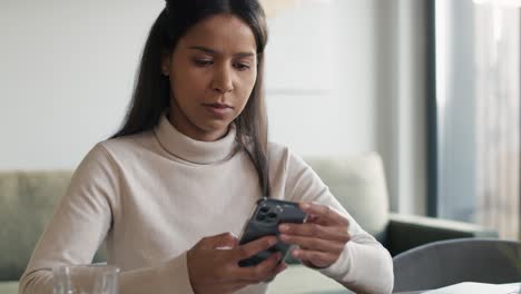 Mixed-race-woman-sitting-at-the-desk-and-browsing-phone