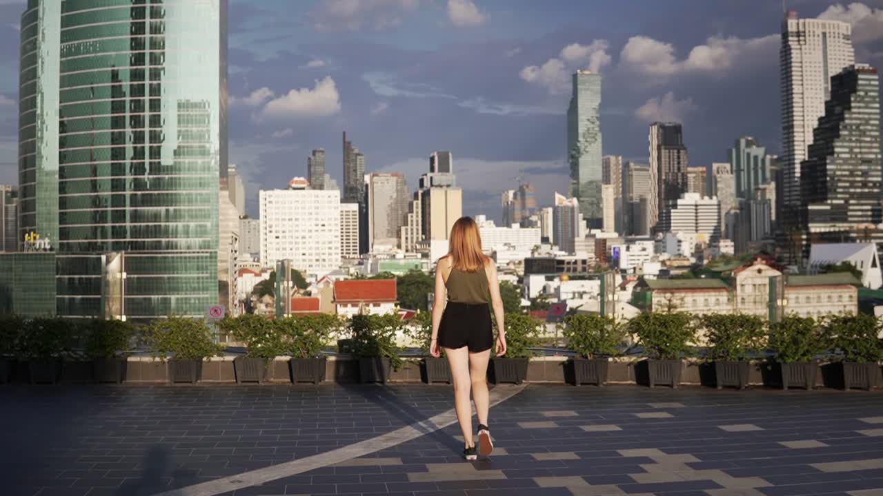 una hermosa mujer joven camina lentamente en un techo, admirando la vista panorámica del horizonte de bangkok