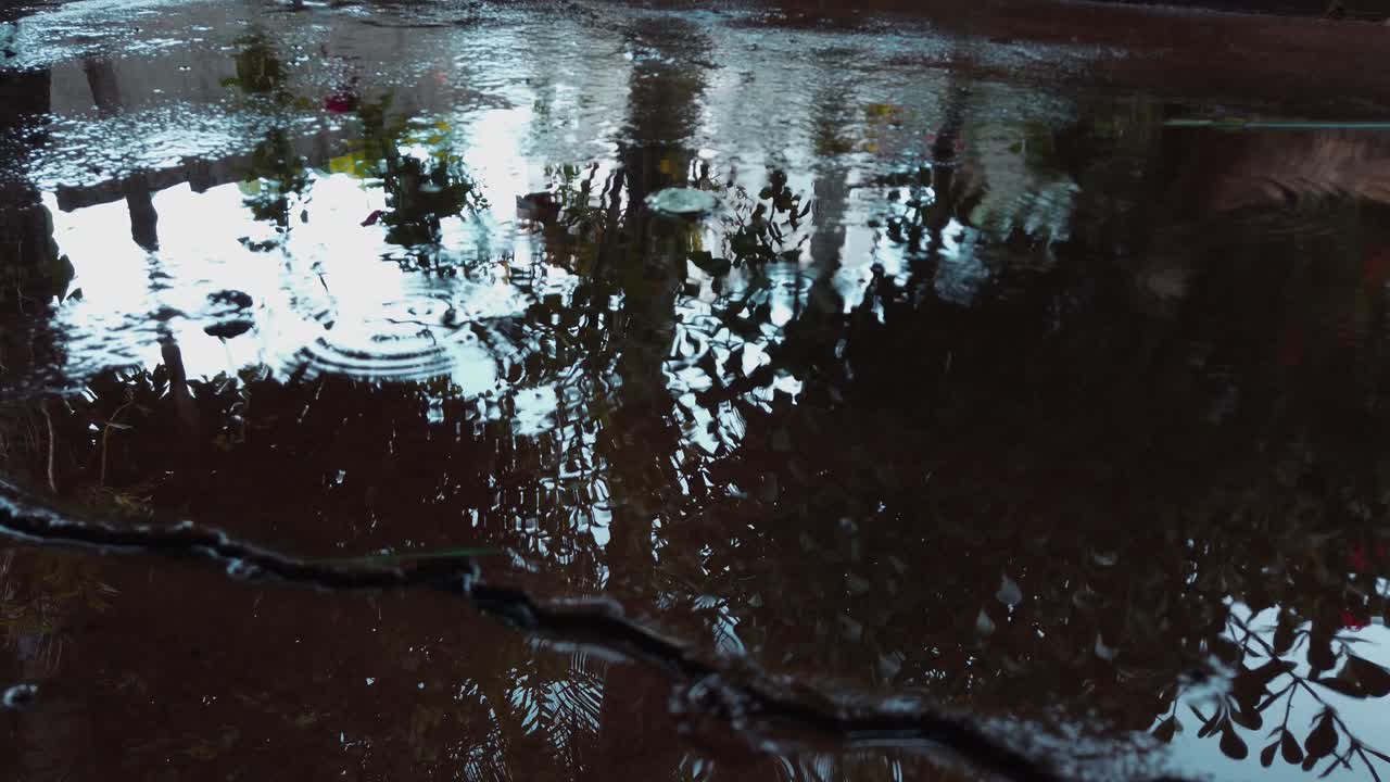 Autumn rain water drops falling into puddle on sidewalk, slow motion close up