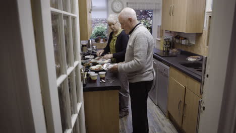 an elderly couple preparing food in the kitchen