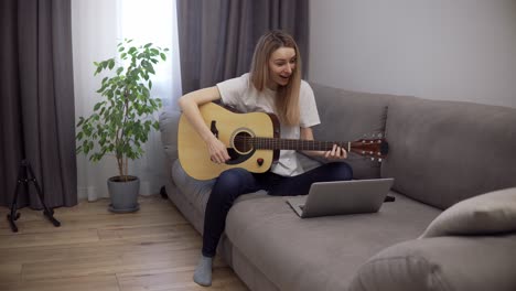 portrait of a woman plays the guitar through a video call on a laptop, leaning chords