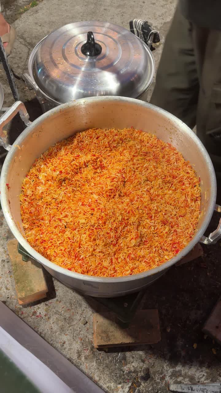 Person øser farverig Biryani-ris fra en stor gryde.