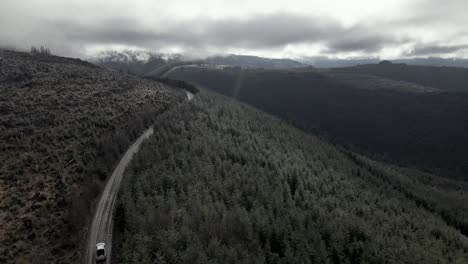 Overtaking-a-single-white-truck-navigating-a-dirt-forest-road-through-land-managed-forest,-aerial