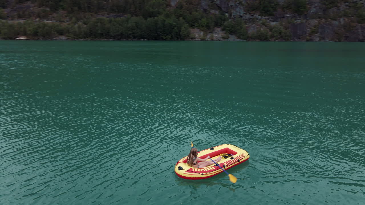 Girando intorno a una ragazza che rema su un piccolo gommone in un lago verde.