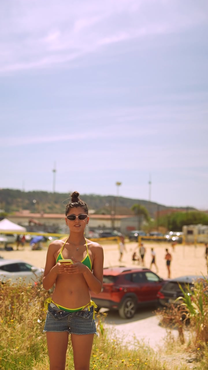 Giovane donna in bikini e pantaloncini che usa lo smartphone all'aperto