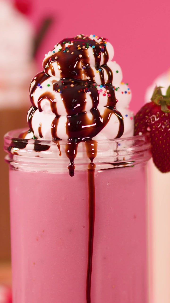 Un frappè alla fragola rosa vivace guarnito con panna montata, sciroppo al cioccolato e codette colorate.