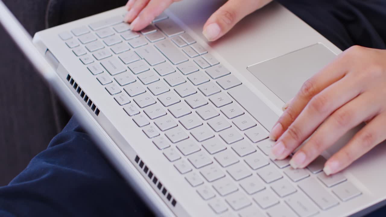 African American woman positioning fingers then typing and using trackpad on silver laptop on lap