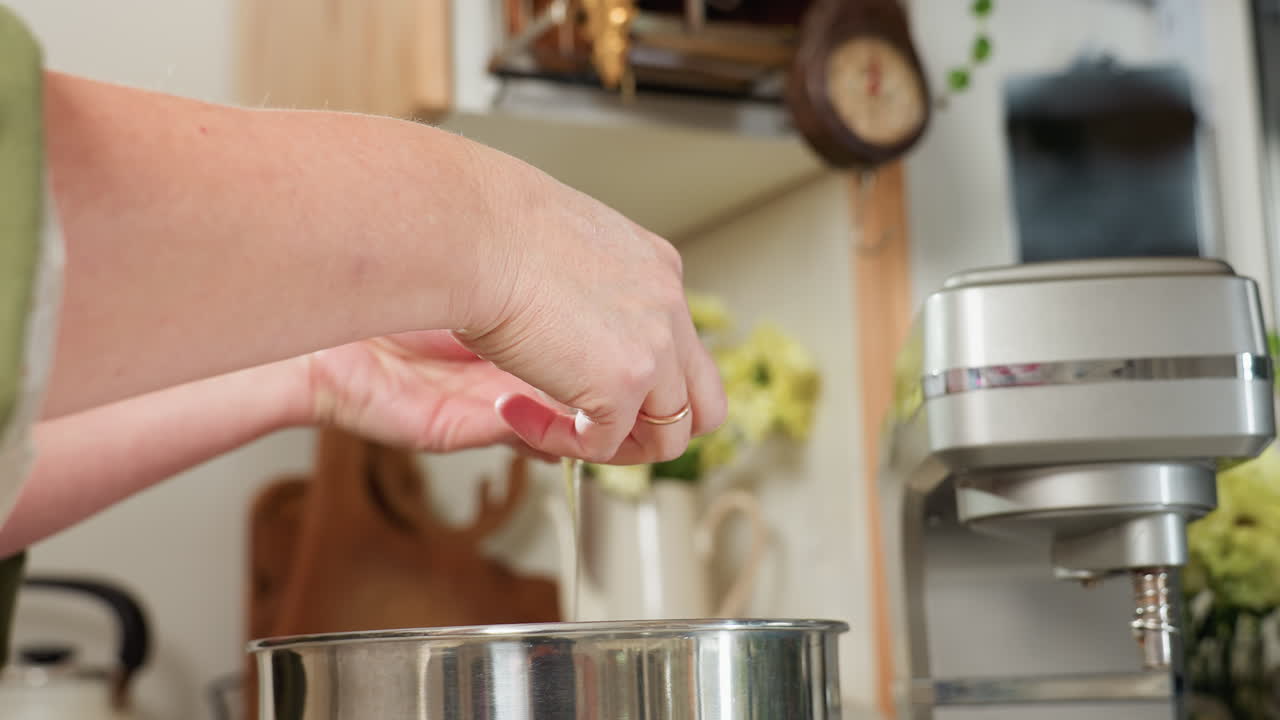 Close up of chef separating egg by carefully pouring egg white into stainless steel bowl while keeping yolk aside in glass cup during kitchen prep