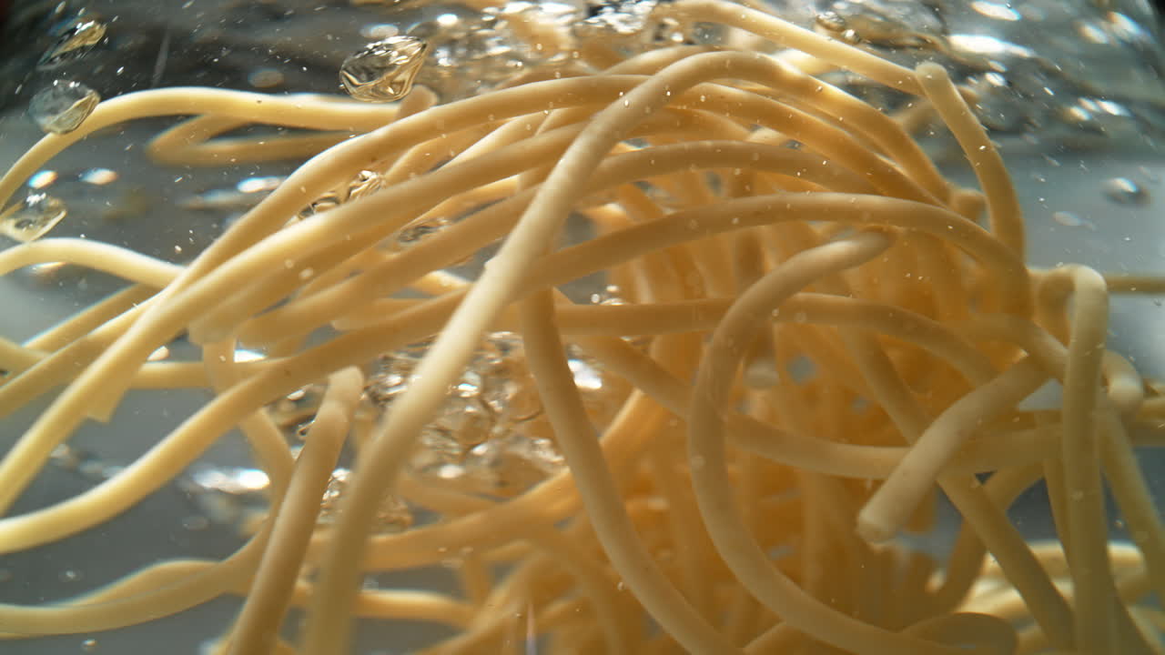 Spaghetti cotti che si muovono nell'acqua bollente, con bolle d'aria che salgono attraverso i fili di pasta - Una vista subacquea.