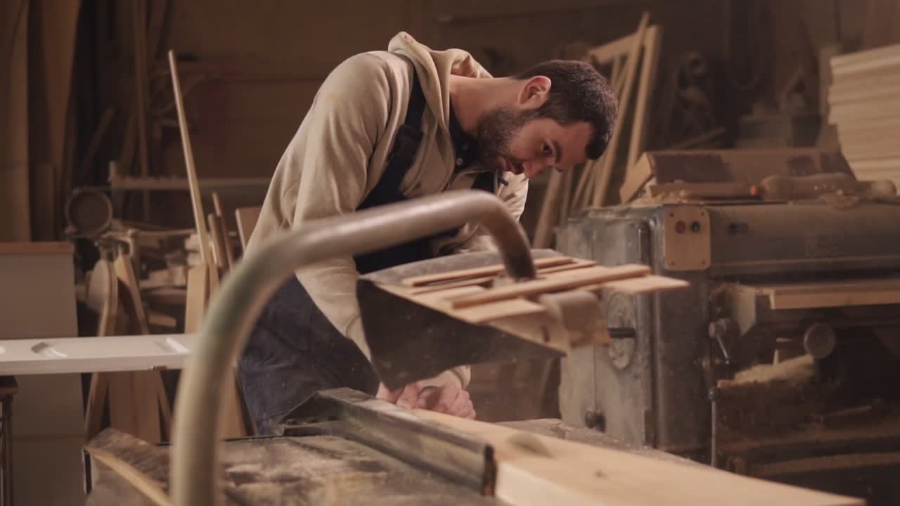 el artesano está trabajando en una sierra eléctrica. cortando una gran barra de madera. el polvo y las astillas se están esparciendo.