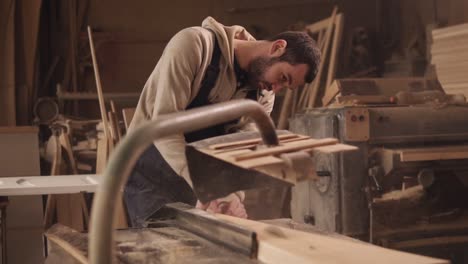 the craftman is working on electric saw machine. sawing a large wooden bar. dust and chips are scattering