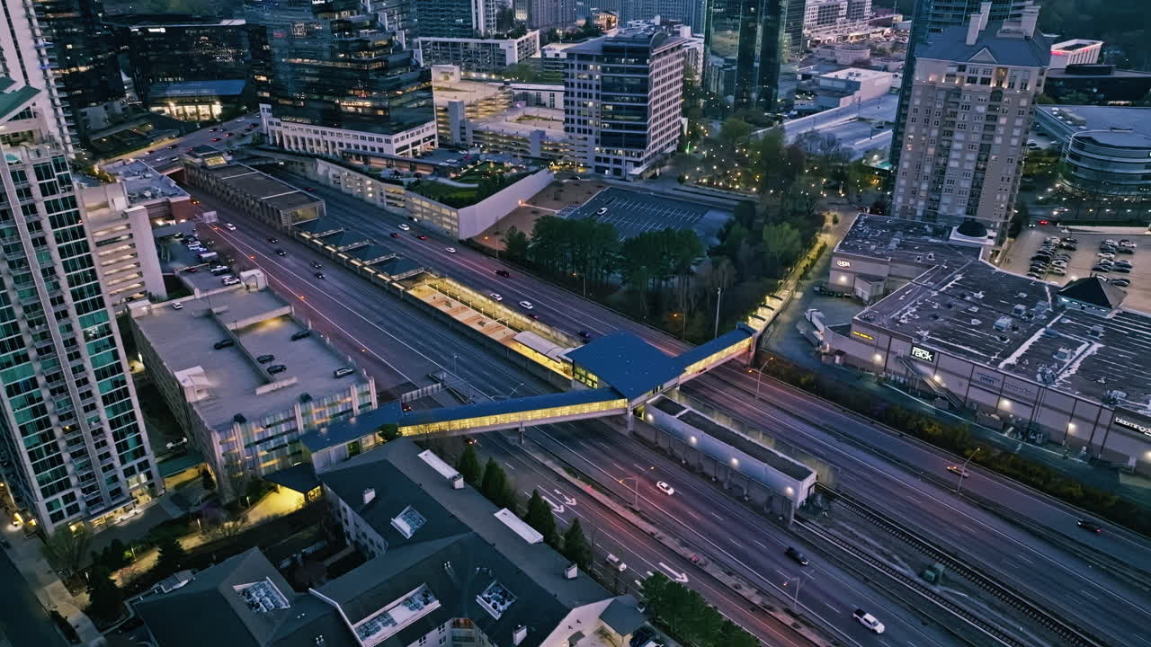 Drone static establishing above cars below metro transit walkway, city blocks and commercial zones in Atlanta Buckhead during sunset light