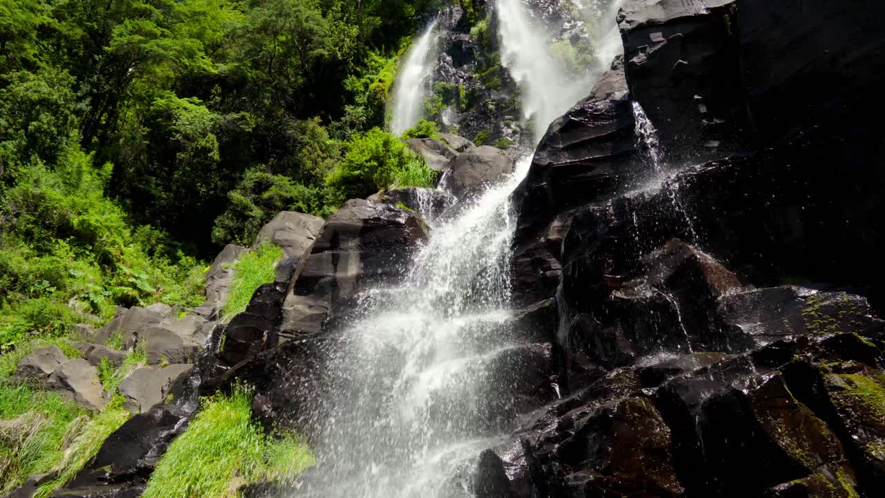 mano de salto niña encantada cascada brumosa que fluye por una pared rocosa rodeada de una densa selva tropical en liquiñe, chile