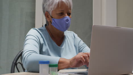 mujer biracial mayor con máscara facial teniendo consulta médica usando una computadora portátil