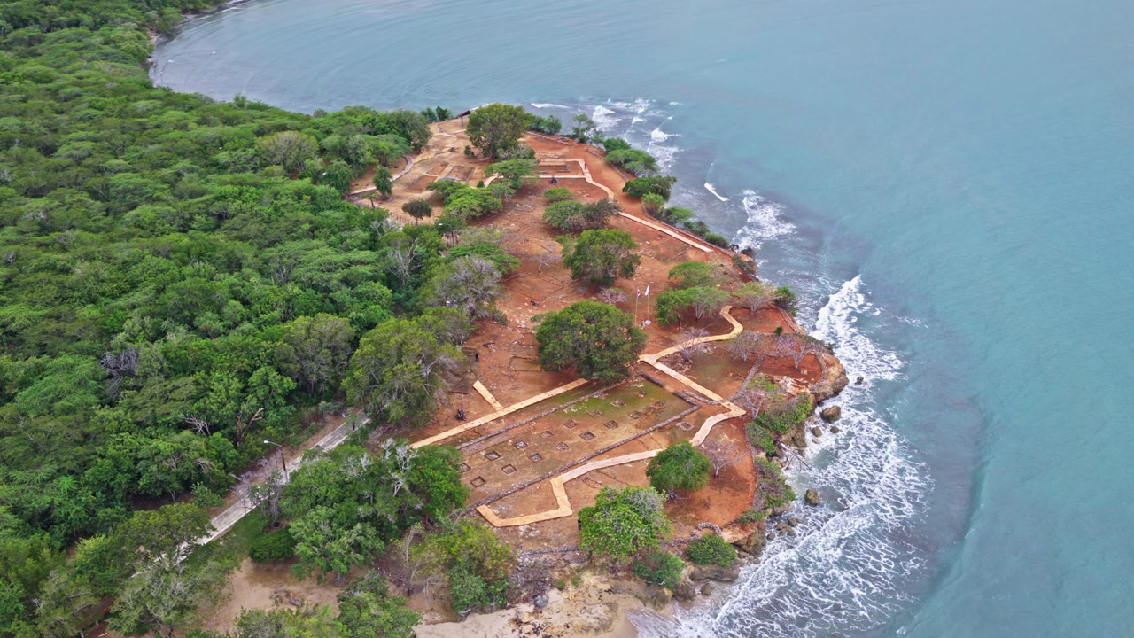 High altitude drone view of La Isabela historical park surrounded by dense forest and the Caribbean Sea in Dominican Republic