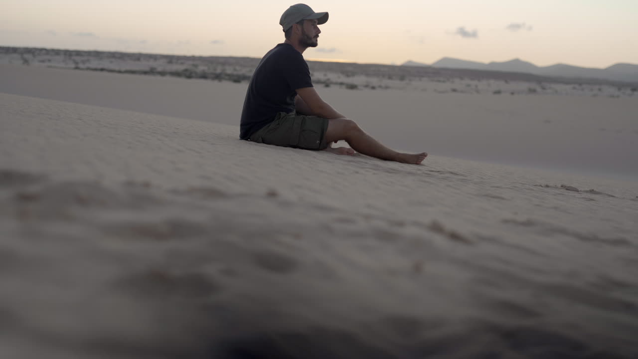 young adventurer barefoot traveller sitting alone in sand desert dunes during sunset, dry scenic landscape in remote mountains Fuerteventura canary island Spain