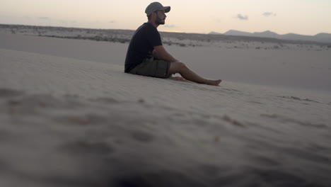 young adventurer barefoot traveller sitting alone in sand desert dunes during sunset, dry scenic landscape in remote mountains fuerteventura canary island spain