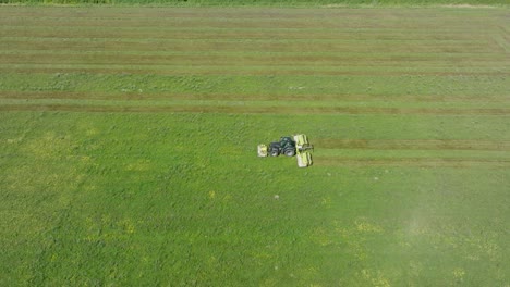 Vista-Aérea-De-Un-Tractor-Cortando-Un-Campo-De-Hierba-Verde-Fresca,-Un-Granjero-En-Un-Tractor-Moderno-Preparando-Comida-Para-Animales-De-Granja,-Un-Día-Soleado-De-Verano,-Un-Gran-Drone-Con-Vista-De-Pájaro-Que-Se-Mueve-Hacia-La-Izquierda