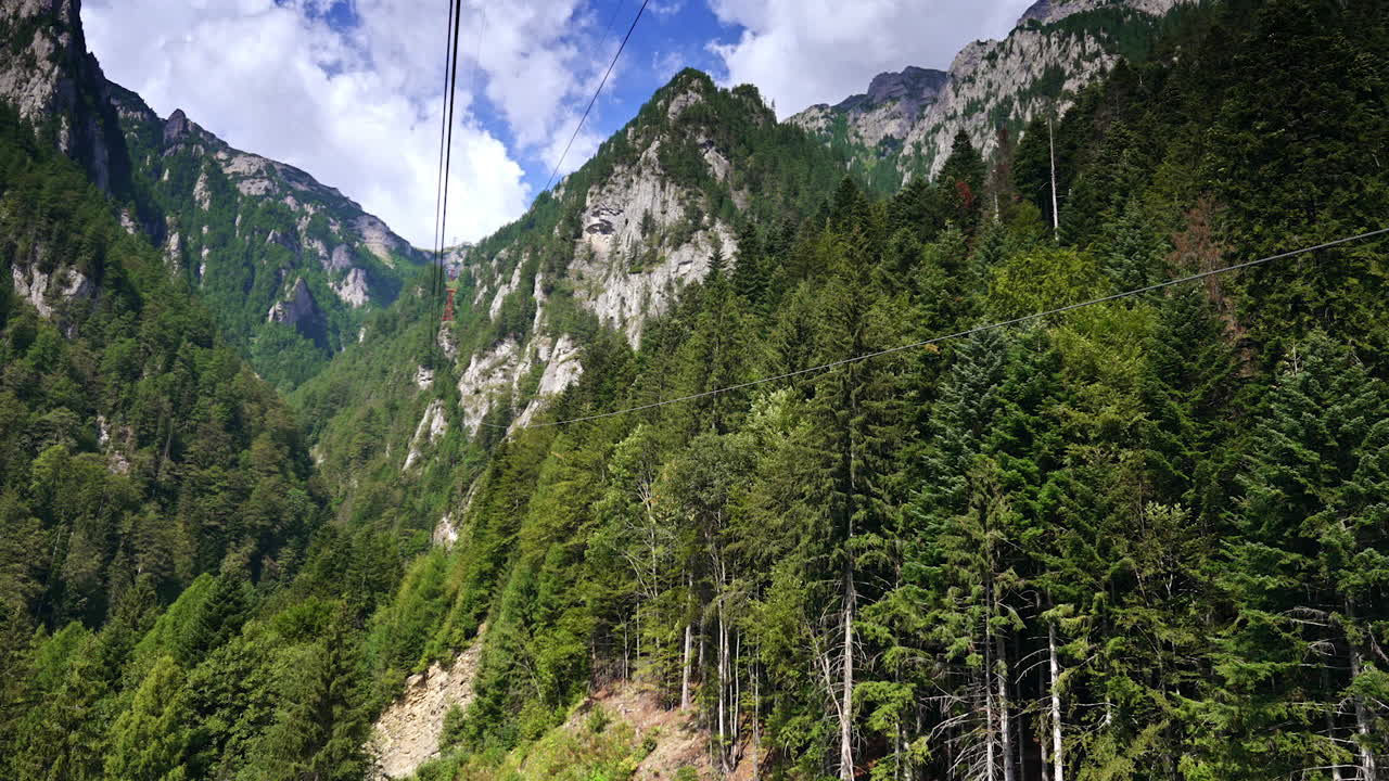 Vista maestosa delle cime delle montagne. Una foresta verde lussureggiante circonda montagne ripide sotto un cielo azzurro brillante con soffici nuvole bianche sopra.