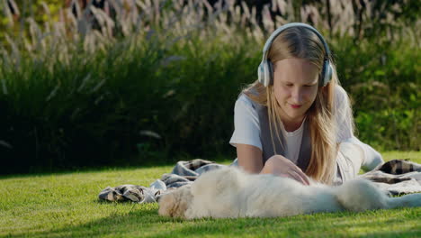 una adolescente juega con un cachorro, se acuesta en el césped, escucha música con auriculares