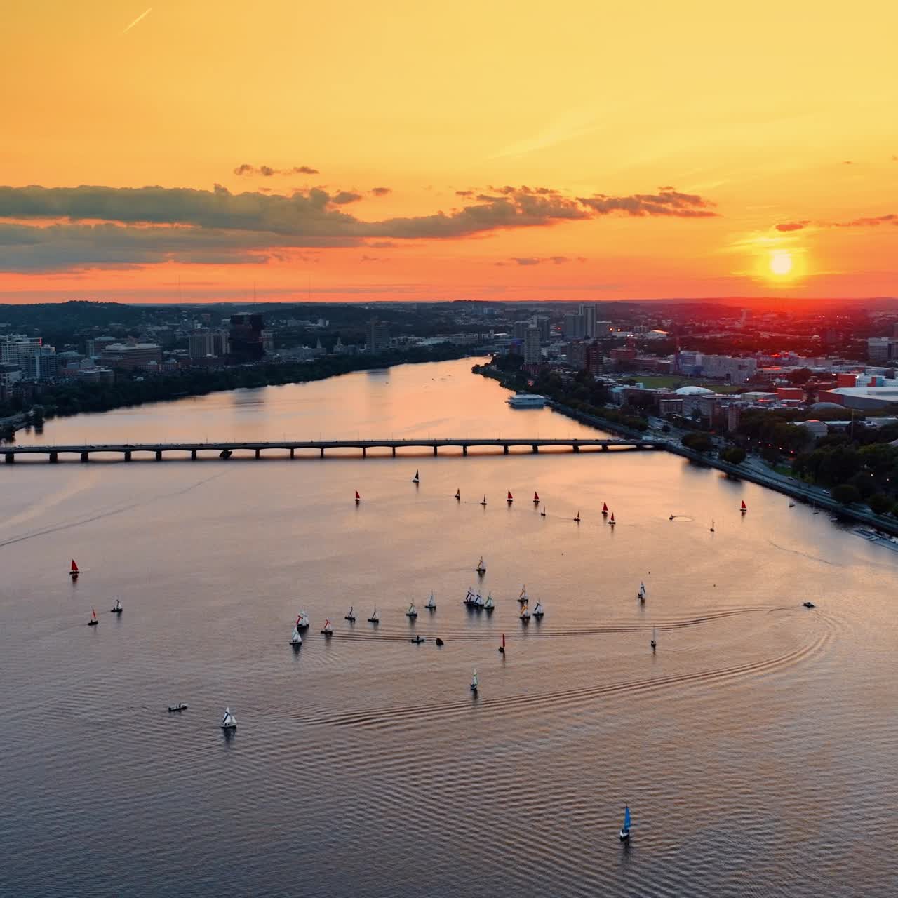 Approaching the group of yachts sailing by the Charles River in Boston, USA. Drone flying above the water. Beautiful orange sky at backdrop